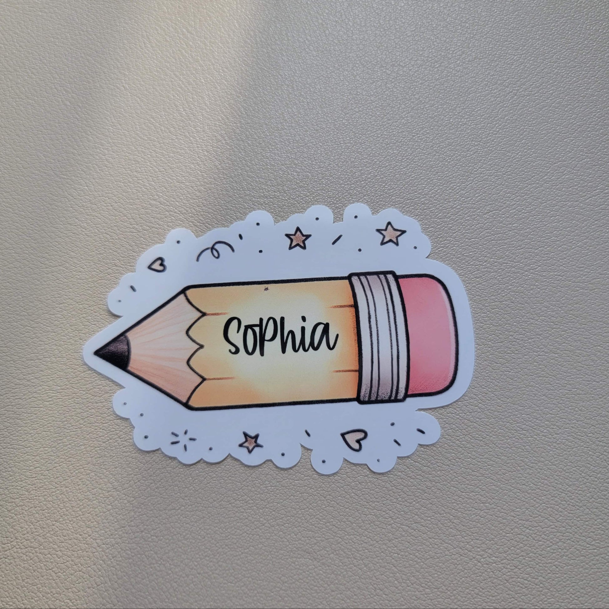 Sticker of a pencil with 'Sophia' on it attached to a textured surface
