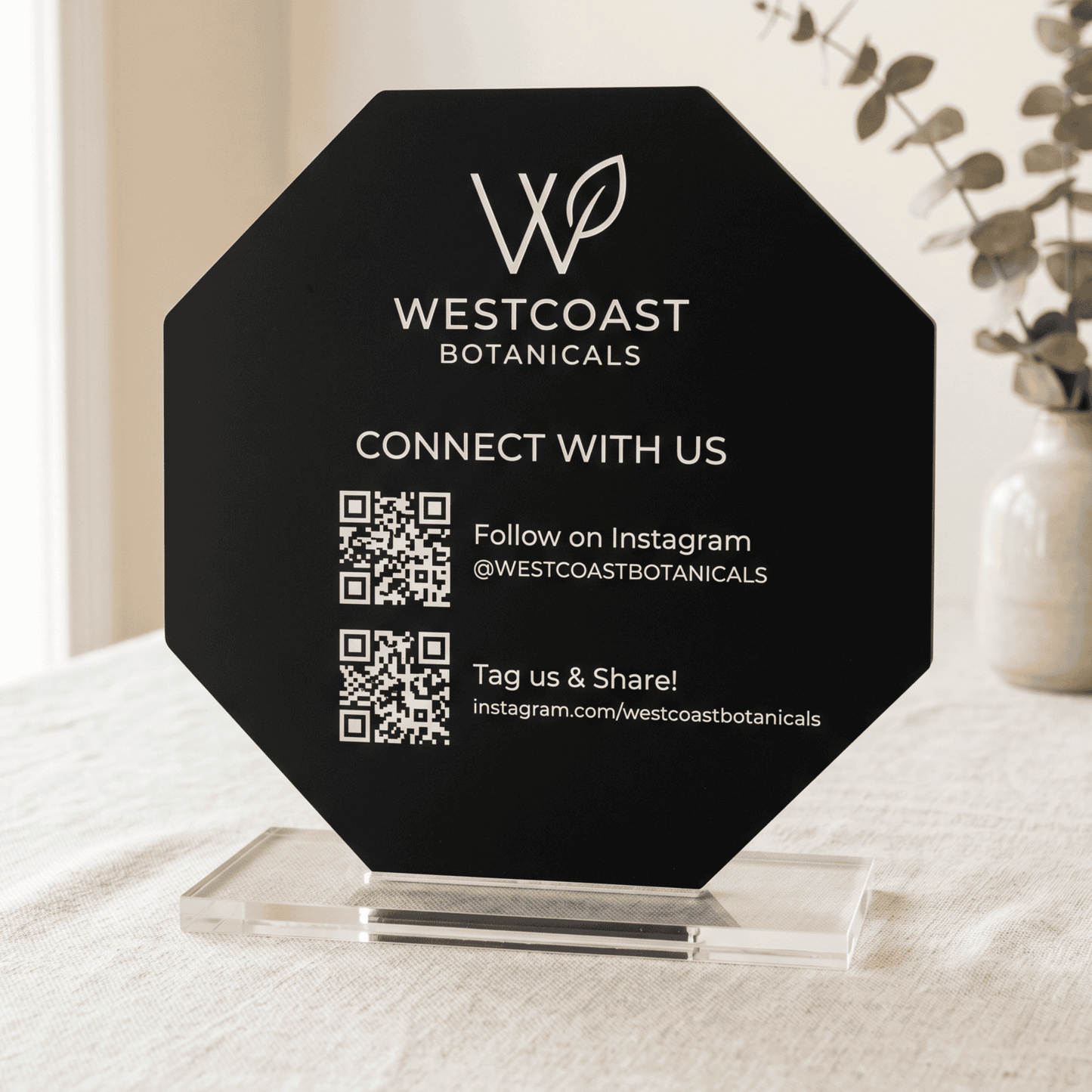 Black octagonal sign with Westcoast Botanicals branding and QR code on a white surface.