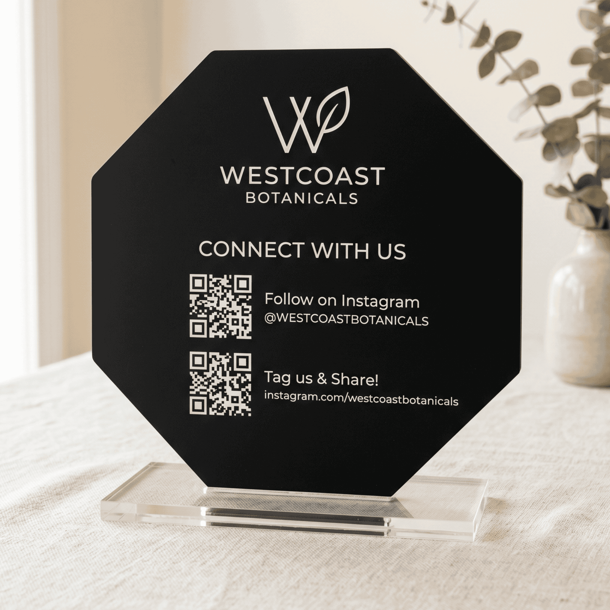 Black octagonal sign with Westcoast Botanicals branding and QR code on a white surface.