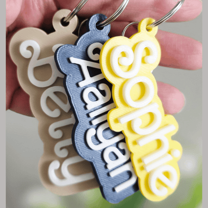 Three personalized keychains with names 'Belu', 'Hannah', and 'Sophie' held by a hand.